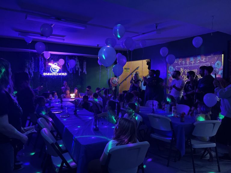 Birthday Party room with green background and purple table decorations and setup. Purple balloons. Light is turned off and birthday child is ready to blow on the candles and the cake.