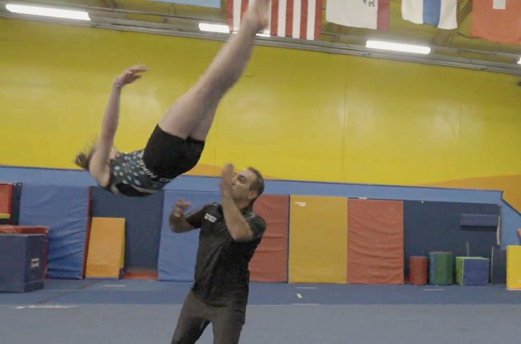 Girl doing a back flip tumbling while coach is spotting her.