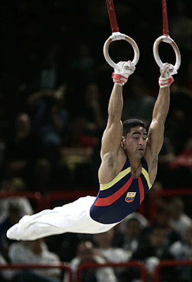 Regulo Carmona on rings wearing blue jersey doing a swing